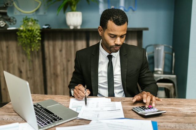 Accountant in a suit using a calculator and writing on tax documents